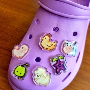Six shoe charms sitting on a purple shoe. The six shoe charms are: Silk worm, junimo, chicken, sheep, stardop, and cow