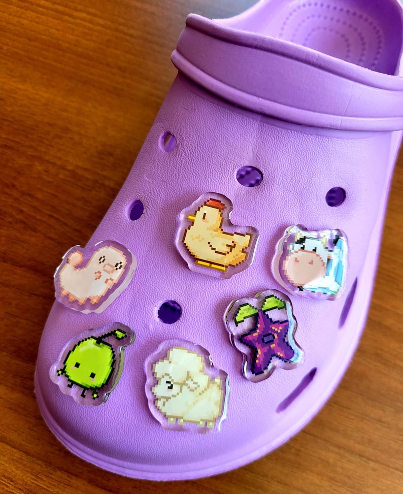 Six shoe charms sitting on a purple shoe. The six shoe charms are: Silk worm, junimo, chicken, sheep, stardop, and cow