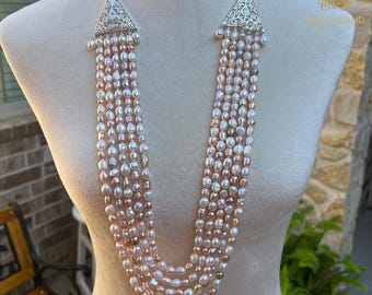 Op de afbeelding: Een meerstrengige parelketting met een zilveren driehoekige hanger. De ketting heeft een verscheidenheid aan roze en witte parels.