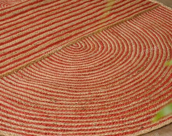 Puede incluir: Una alfombra de forma ovalada fabricada con fibras de yute natural trenzadas. La alfombra presenta un patrón repetitivo de círculos concéntricos y líneas paralelas en bandas alternas de color beige y naranja vibrante.
