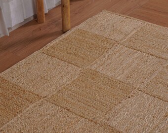 Puede incluir: Una alfombra rectangular hecha de fibras de yute natural de color tostado, con un patrón de cuadrícula de secciones cuadradas cosidas. La alfombra tiene una textura tejida gruesa y un color marrón claro consistente en toda su superficie.