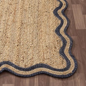 Könnte beinhalten: Ein natürlicher Jute-Teppich mit gewelltem, wellenförmigem Rand. Der Teppich hat eine hellbraune Farbe mit einem dunkelblauen Rand. Der Teppich besteht aus gewebten Jute-Fasern und liegt auf einem Holzboden.