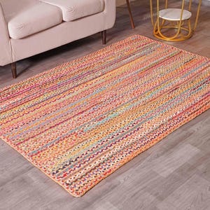 May include: A rectangular, multi-colored braided rug with a striped pattern. The rug features a mix of orange, pink, yellow, and blue hues. It is placed on a wooden floor, and a beige sofa is partially visible in the background.