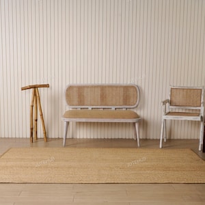 May include: A natural fiber jute rug is laid on a light wood floor. A wooden bench with a woven back and seat, a matching chair, and a crib are in the background. A bamboo tripod stand is on the left.
