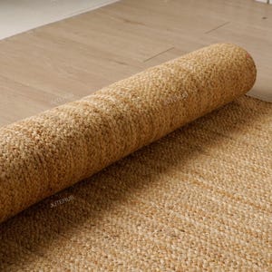May include: A rolled-up, natural-toned jute rug rests on a light-colored wooden floor. The rug's texture is visible, showcasing its woven construction. The unrolled portion of the rug lies flat, revealing the full weave pattern. The rug is a neutral color, suitable for various interior styles.
