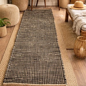 May include: A rectangular runner rug featuring a dense, repeating black and beige checkered pattern. The rug has a thick, textured weave with a solid beige border along the edges, laid flat on a light brown wooden floor surface.