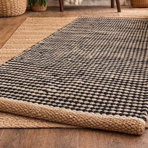 May include: A rectangular area rug featuring a woven texture with a repeating pattern of black and natural tan fibers. The rug has a thick, braided border in a solid natural tan color, creating a distinct contrast against the central pattern.