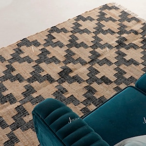 May include: A rectangular jute rug with a geometric pattern in black and tan. The rug has a fringed edge and is next to a teal sofa. The rug's design is a repeating series of angular shapes.