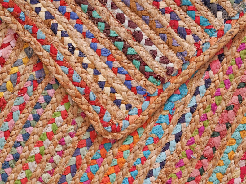 May include: Close-up of a colorful braided jute rug. The rug features a mix of vibrant colors including red, blue, green, and pink, woven into a textured pattern. The natural jute fibers provide a warm, earthy tone.