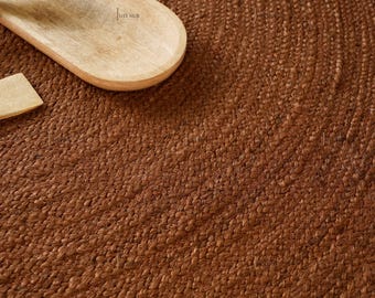 Könnte beinhalten: Nahaufnahme eines gewebten braunen Jute-Teppichs mit natürlicher Textur. Ein hölzerner Servierlöffel und ein kleiner Holzspatel sind teilweise in der oberen linken Ecke zu sehen. Die Oberfläche des Teppichs ist detailliert.