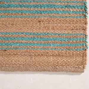 Op de afbeelding: Close-up van een natuurvezel tapijt met horizontale strepen. Het tapijt heeft afwisselende banden van bruin en turquoise blauw. De textuur van het tapijt is zichtbaar, waaruit de geweven constructie blijkt. De rand van het tapijt is zichtbaar.