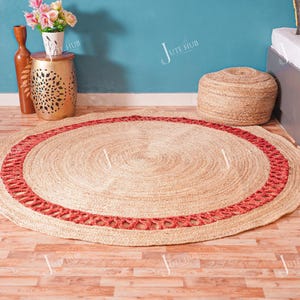 Op de afbeelding: Een ronde jute vloerkleed met een rode rand. Het vloerkleed is gemaakt van natuurlijke vezels en heeft een geweven ontwerp. Het vloerkleed heeft een diameter van ongeveer 152 cm, geschikt voor een woon- of slaapkamer.