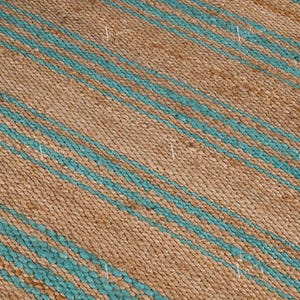 Op de afbeelding: Close-up van een geweven tapijt met een natuurlijke bruine achtergrond en diagonale strepen in turquoise blauw. Het tapijt heeft een textuur en de strepen zijn gelijkmatig verdeeld.