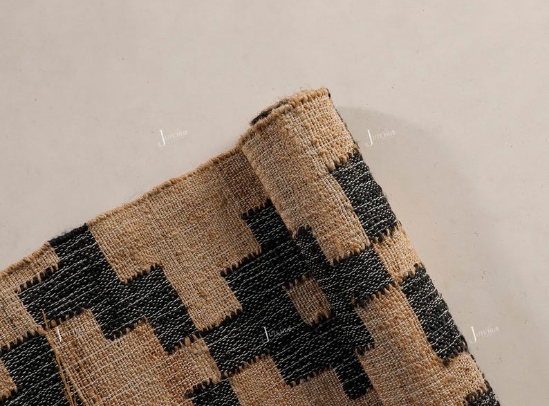 May include: A rolled-up rug with a geometric pattern in natural tan and black. The rug's design features a repeating zigzag pattern. The rug is made of a woven material, possibly jute or a similar fibre.