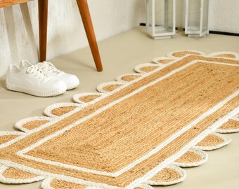 Puede incluir: Una alfombra rectangular tipo pasillero hecha de fibra de yute natural color canela, con un panel central rectangular bordeado por una línea cosida blanca y un acabado de borde festoneado que alterna entre yute canela y detalles en tela blanca.
