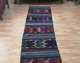 May include: A colourful, handwoven runner rug with a black background and intricate geometric patterns in shades of red, blue, green, and yellow. The rug has a fringed edge and is approximately 2.5 metres long.