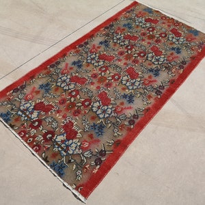 Puede incluir: Una alfombra floral vintage con un borde rojo y un fondo beige. La alfombra presenta un patrón repetitivo de flores azules, rojas y blancas.