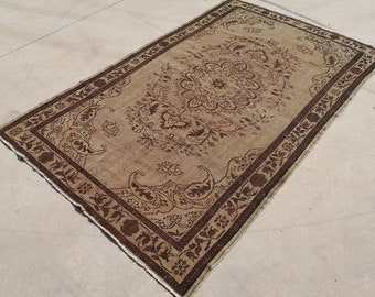 May include: A rectangular, vintage-style rug with a central floral medallion design in shades of brown and beige. The rug features a dark brown border with intricate patterns and a fringed edge, suitable for home decor.