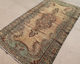 May include: A vintage rug with a beige background and intricate floral patterns in shades of green, brown, and red. The rug has a fringed edge.
