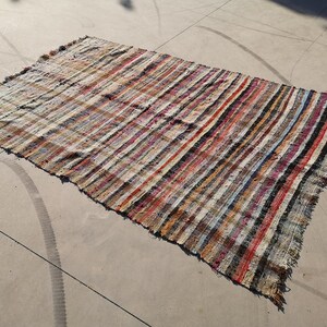 May include: A striped rug with a variety of colors, including red, blue, and white. The rug is made of a woven material and has a frayed edge.