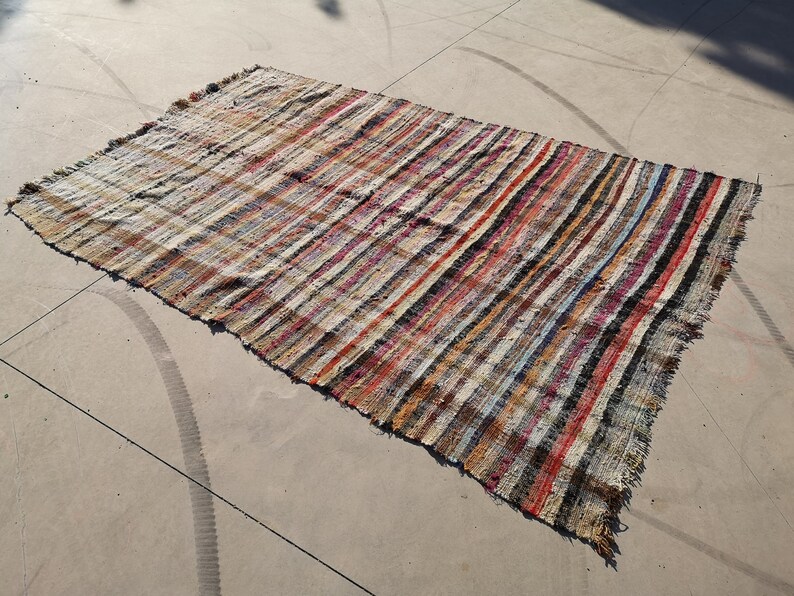 May include: A striped rug with a variety of colors, including red, blue, and white. The rug is made of a woven material and has a frayed edge.