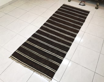May include: A long, narrow, brown and white striped rug with a fringed edge. The rug is made of a woven material and has a traditional design.