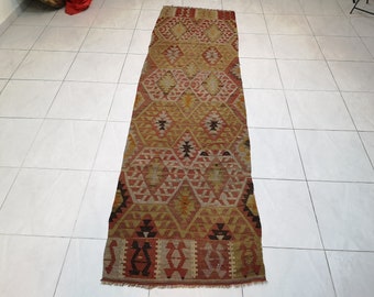 May include: A long, rectangular rug with a traditional Turkish kilim pattern. The rug is woven with a variety of colors, including red, orange, yellow, and brown. The rug has a fringe on both ends.