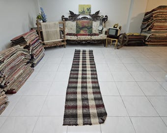 May include: A long, rectangular, black, white, and red striped rug with a fringe border. The rug is laid out on a white tiled floor.