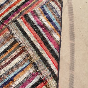 May include: A colorful striped rag rug with a frayed edge. The rug is made of recycled materials and has a rustic, handmade look.