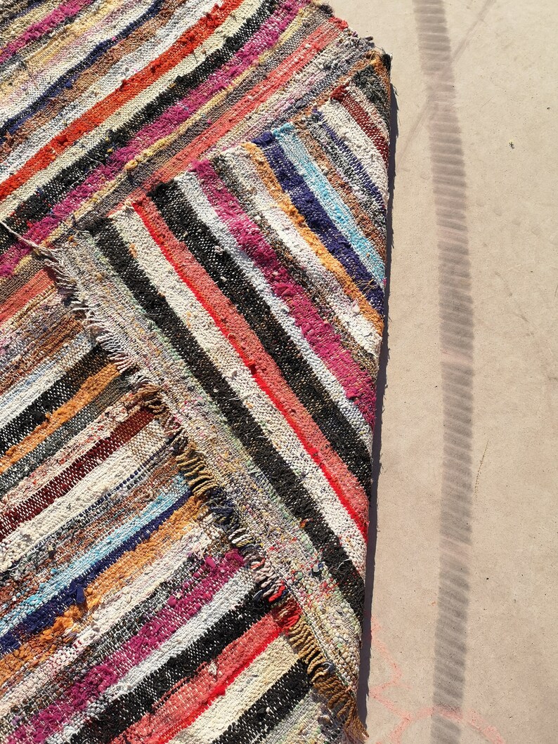 May include: A colorful striped rag rug with a frayed edge. The rug is made of recycled materials and has a rustic, handmade look.