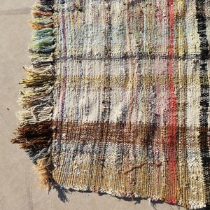 May include: A handwoven rug with a brown, white, and red striped pattern. The rug has a fringe border and is made of recycled materials.
