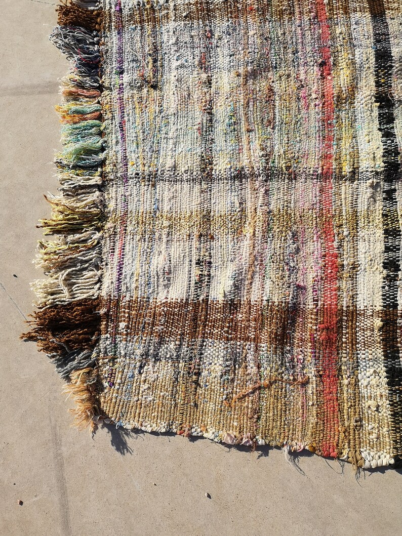 May include: A handwoven rug with a brown, white, and red striped pattern. The rug has a fringe border and is made of recycled materials.