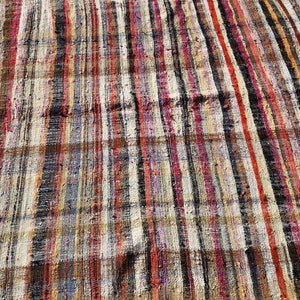 May include: A colorful striped rug with a variety of colors, including red, blue, yellow, and black. The rug is made of woven fabric and has a rustic, vintage look.