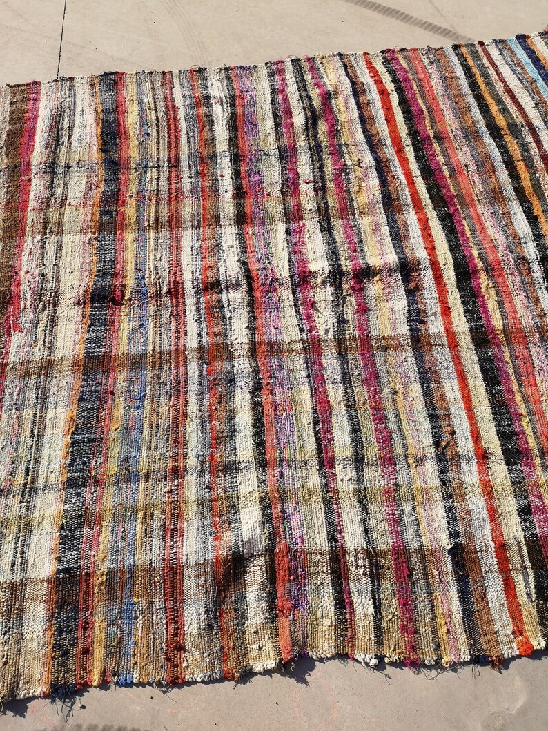 May include: A colorful striped rug with a variety of colors, including red, blue, yellow, and black. The rug is made of woven fabric and has a rustic, vintage look.
