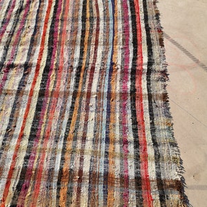 May include: A colorful striped rug with a variety of colors, including red, orange, yellow, green, blue, purple, and black. The rug is made of woven fabric and has a frayed edge.