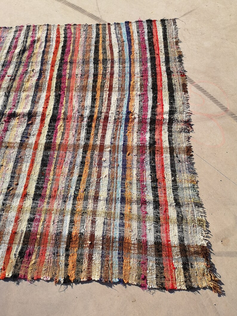 May include: A colorful striped rug with a variety of colors, including red, orange, yellow, green, blue, purple, and black. The rug is made of woven fabric and has a frayed edge.