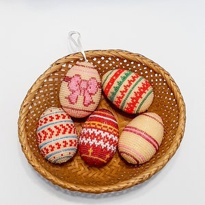 May include: Five beaded Easter eggs in a woven basket. The eggs are decorated with different patterns in red, white, green, and pink.