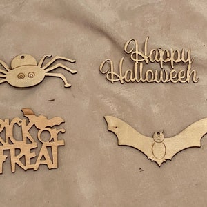 May include: Four wooden Halloween cutouts: a spider, the words "Happy Halloween", the words "Trick or Treat", and a bat. The cutouts are made of light-colored wood and are suitable for crafting or decoration.