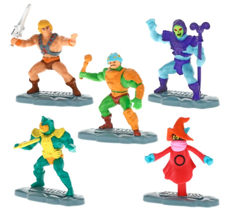 May include: A set of six Masters of the Universe action figures. The figures are made of plastic and are painted in bright colors. The figures include He-Man, Skeletor, Man-At-Arms, Beast Man, Teela, and Evil-Lyn. Each figure stands on a small plastic base.