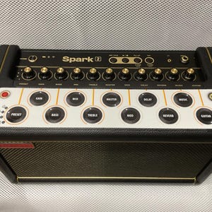 May include: A black and gold Spark 2 guitar amplifier, featuring numerous knobs and buttons for sound adjustment. The amplifier includes a speaker grill and a white control panel with labels such as Gain, Bass, and Treble. Designed for guitarists.