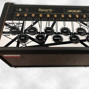 Könnte beinhalten: Schwarzer und weißer Gitarrenverstärker mit einem grafischen Design auf der Vorderseite. Der Verstärker verfügt über Knöpfe für Gain, Bass, Höhen, Mitten, Master, Delay, Reverb und Ausgang. Der Text "Spark 40" ist auf der Vorderseite des Verstärkers aufgedruckt.