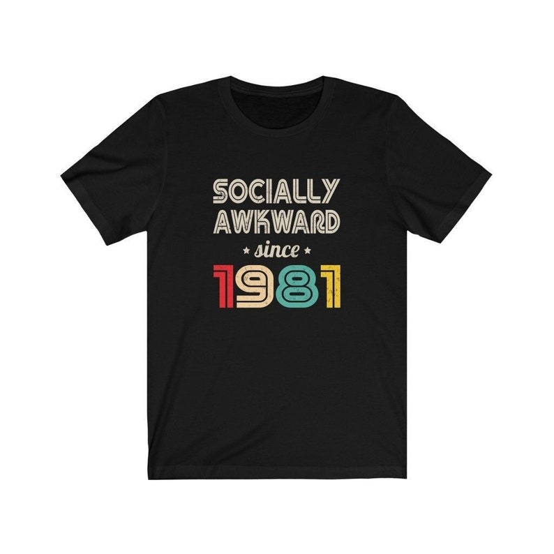 May include: Black t-shirt with white text that reads "Socially Awkward since 1981". The year is in colorful retro font.