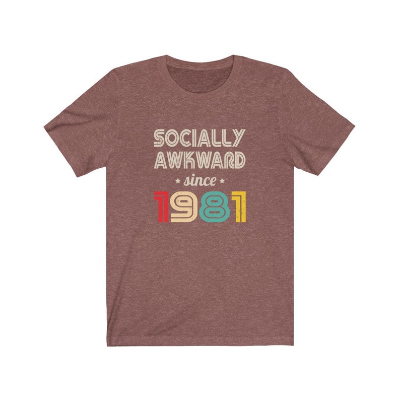 May include: A heather brown t-shirt with the text "Socially Awkward since 1981" in a retro font with colorful numbers.