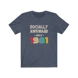 May include: A navy blue t-shirt with the text "Socially Awkward since 1981" in a retro style font. The numbers are in different colors: red, yellow, green, and blue.