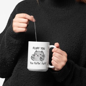 May include: White ceramic mug with a black and gray cartoon cat with the text "Fluff You You Fluffin' Fluff" printed on it.