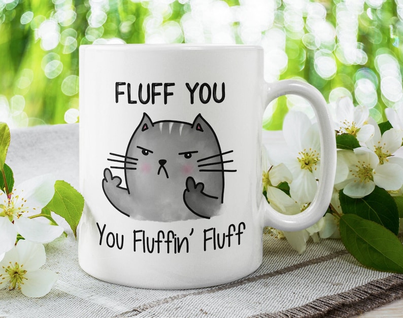 May include: White ceramic mug with a gray cat illustration giving the middle finger. The text on the mug reads "Fluff You You Fluffin' Fluff".