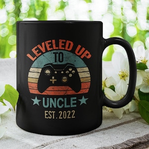 Könnte beinhalten: Schwarze Kaffeetasse mit einem weißen Design, auf dem "Leveled Up To Uncle Est. 2022" mit einem Retro-Videospiel-Controller-Grafik steht.