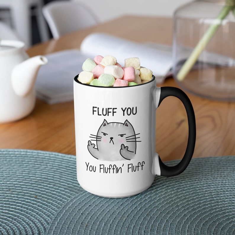 May include: White ceramic mug with a black handle. The mug has a cartoon cat with the text "Fluff You You Fluffin' Fluff" printed on it.