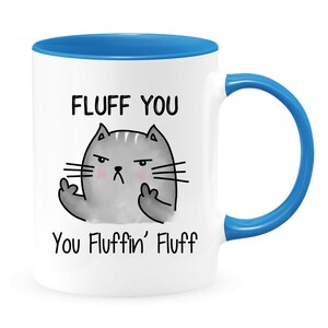 May include: White ceramic coffee mug with a blue rim and handle. The mug features a cartoon cat with a grumpy expression and the text "FLUFF YOU You Fluffin' Fluff".