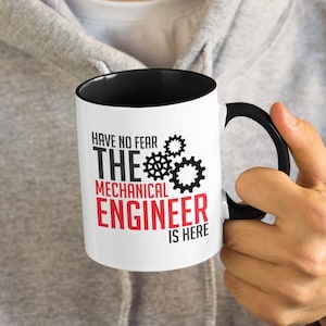 Puede incluir: Taza de cerámica blanca con borde y asa negros. La taza tiene un gráfico en blanco y negro de engranajes con el texto "Have no fear, the mechanical engineer is here" en negro y rojo.